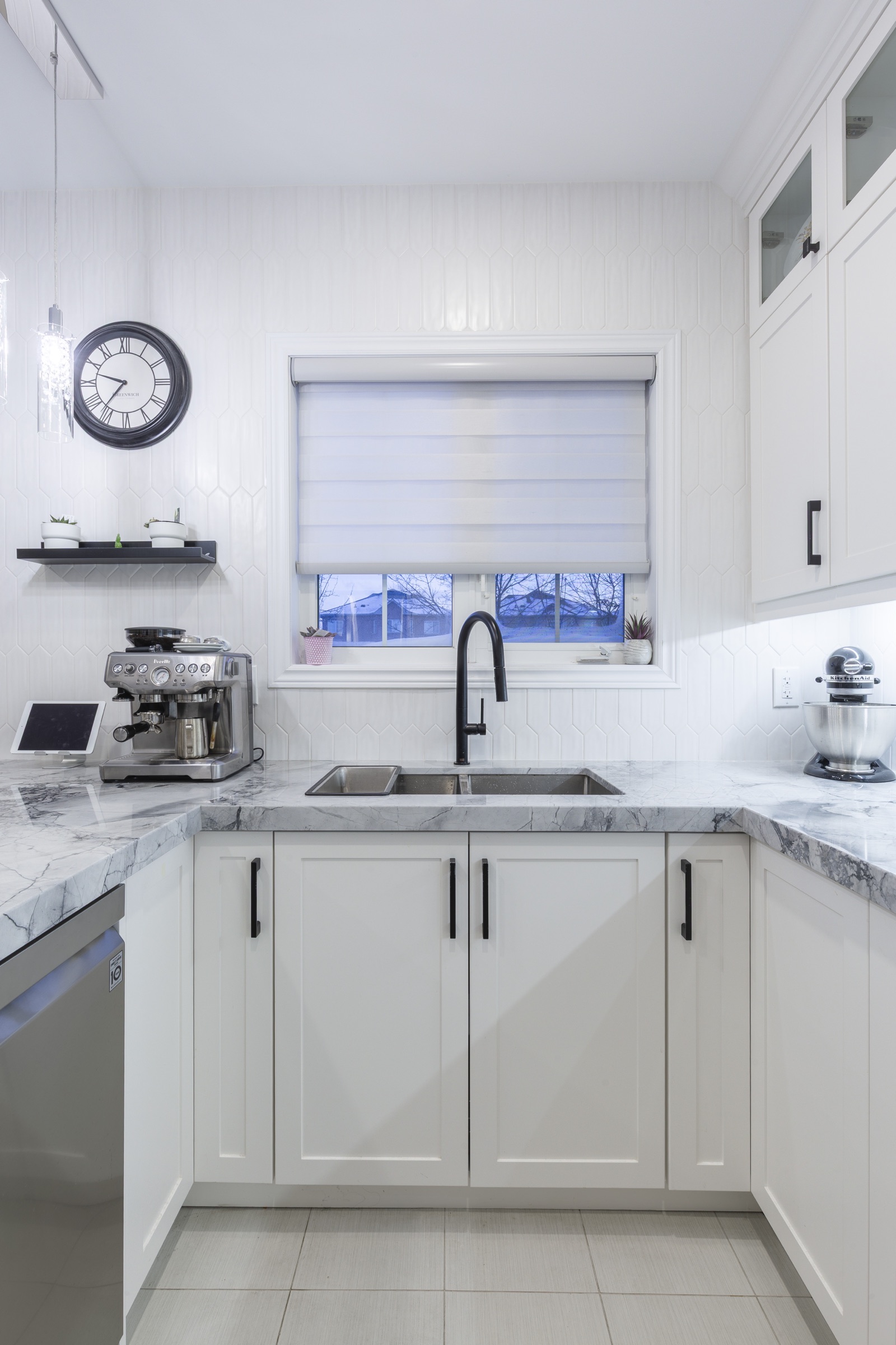 White cabinets, veined countertop and dark faucet beneath a window