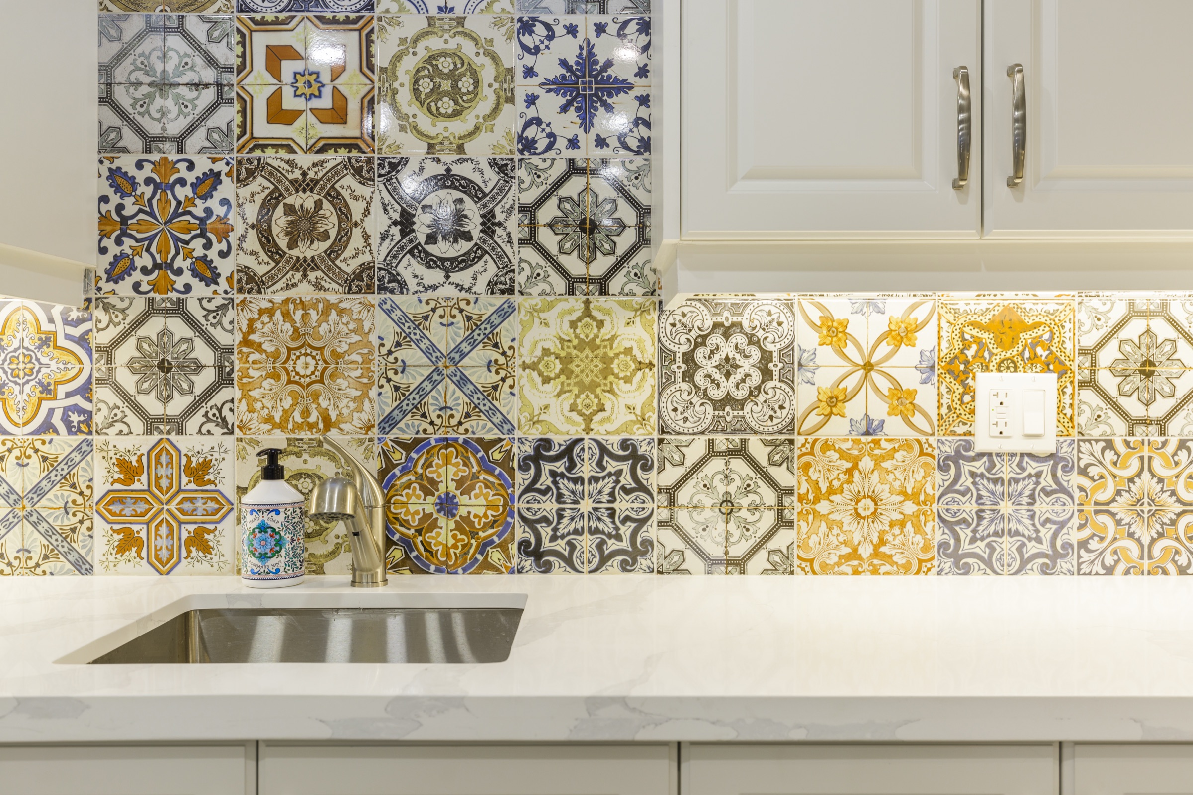 Multicoloured patterned tiles behind a sink and cream cabinets
